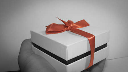 Gift in hand. White box with a red ribbon.