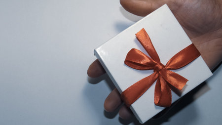 Gray background. Gift with a red ribbon. Gift in hand. White box with red ribbon.の写真素材