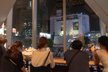 Shibuya, Tokyo, Japan - April 30, 2018: People sitting in coffee shop, watching Shibuya crosswalk in Tokyo, Japan. Shibuya Crossing is one of the busiest crosswalks in the world.