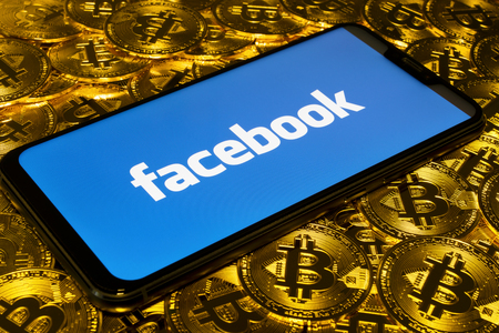 Gold Bitcoin coins pile with the Facebook logo on smartphone screenのeditorial素材
