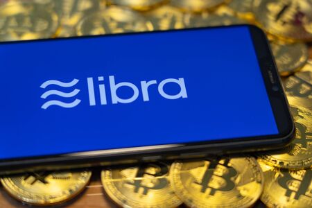 Gold Bitcoin Coins pile with the Facebook's Libra Crypto Coin logo on smartphone screen.のeditorial素材