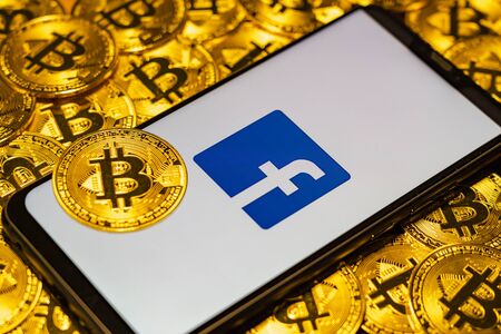 Gold Bitcoin coins pile with the Facebook logo on smartphone screen.のeditorial素材