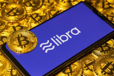 Gold Bitcoin coins pile with the libra logo on smartphone screen.のeditorial素材