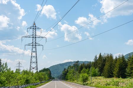 Electricity transmission power lines High voltage tower on green nature endless asphalt road in a rural area.の写真素材