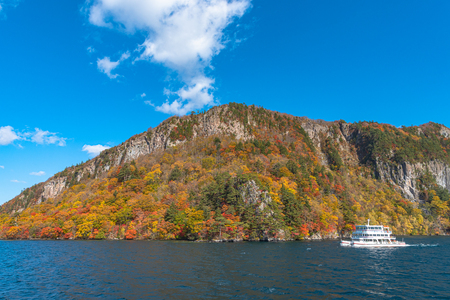 Lake Towada Sightseeing Cruises. Beautiful view, clear blue sky, white cloud, cruise ship in sunny day with autumn foliage season background. Aomori, Japan. Text in Japanese on ship "Third Hakkoda"のeditorial素材