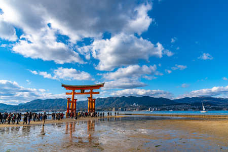 Floating red giant Grand O-Torii gate stands in Miyajima island bay beach at low tide on sunny day. New Year Hatsumode in Itsukushima Shrine, Hiroshima City. Hiroshima Prefecture, Japanのeditorial素材