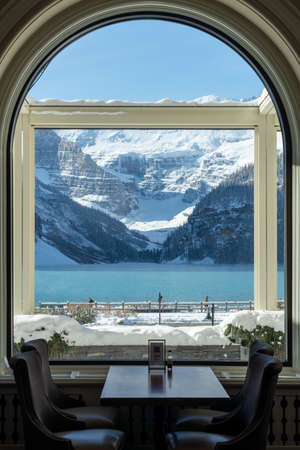 Fairmont Chateau Lake Louise in early winter sunny day morning. Mist floating on turquoise color water surface. Clear blue sky, snow capped mountains in background.のeditorial素材
