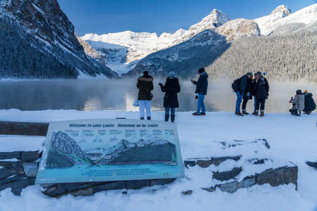 Tourists sightseeing at Lake Louise in early winter sunny day morning. Clear blue sky, snow capped mountains in background. Beautiful landscape in Banff National Park.のeditorial素材