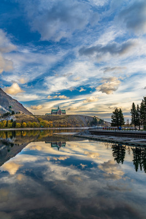 Waterton Lakes National Park lakeshore in autumn foliage season morning. Blue sky, colourful clouds reflect on lake surface like a mirror in sunrise. Fall color landscape. Landmarks in Alberta, Canadaのeditorial素材