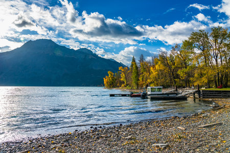 Waterton Middle Lake boat launch in autumn foliage season sunny day morning. Sunlight passing blue sky and clouds on mountains. Waterton Lakes National Park, Alberta, Canada.のeditorial素材