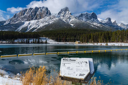 Canmore, AB, Canada-OCT 24 2020: Rundle Forebay Reservoir in winter sunny day morning. Clear blue sky, snow capped Mount Lawrence Grassi mountain range in background.のeditorial素材
