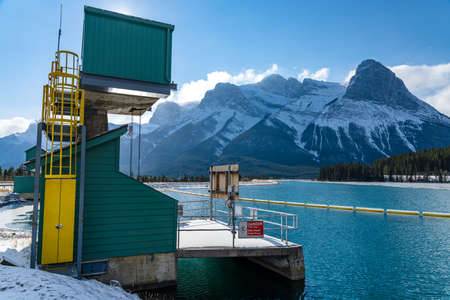 Canmore, AB, Canada-OCT 24 2020: Rundle Forebay Reservoir in winter sunny day morning. Clear blue sky, snow capped Mount Lawrence Grassi mountain range in background.のeditorial素材
