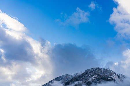 Snowy mountain peak surrounded by clouds in a sunny day morning with blue sky.の写真素材