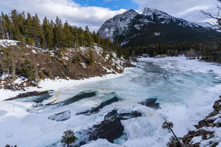 Frozen Bow Falls and Bow River in winter, snowcapped Canadian Rockies in the background. Beautiful scenery in Banff National Park, Alberta, Canada.の写真素材