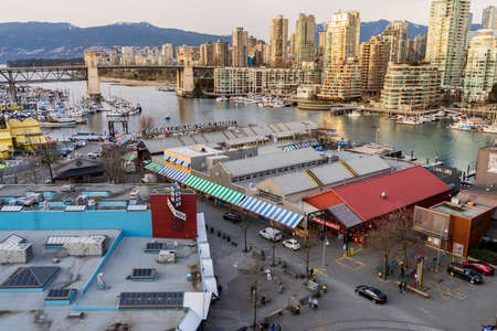 Vancouver, Canada - MAR 11 2021 : Granville Island Public Market and marina in dusk. Vancouver city buildings skyline and Burrard Street Bridge in the background.のeditorial素材