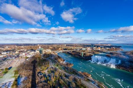 Niagara Falls City, Ontario, Canada - December 19 2021 : Overlooking the Niagara River Rainbow Bridge and American Falls in a sunny day.のeditorial素材