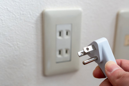 A Japanese wall socket without earth post. 3 pins power plug holding by hand.の写真素材