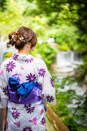 Back view of one woman wearing Japanese yukata summer kimono walking on the road next to the forest waterfall in nature. Kyoto, Japan.の写真素材