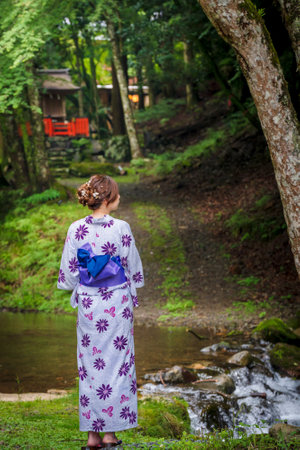 Back view of one woman wearing Japanese yukata summer kimono standing next to a river in Kyoto nature forest. Kyoto, Japan.の写真素材