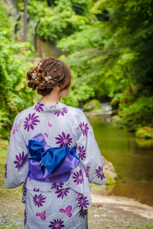 Back view of one woman wearing Japanese yukata summer kimono standing next to a river in Kyoto nature forest. Kyoto, Japan.の写真素材