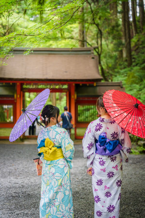 Back view of two women wearing Japanese yukata summer kimono and holding Japanese traditional oil paper umbrella in Kifune Shrine nature forest gate, Kyoto, Japan.の写真素材