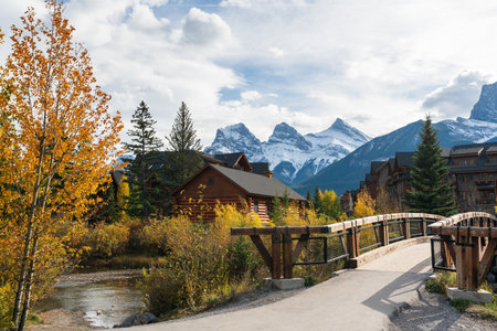 Town of Canmore in fall season. Alberta, Canada. Canmore Opera House at Spring Creek beside the wooden boardwalk bridge. The Three Sisters trio of peaks in the background.のeditorial素材
