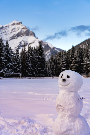 A smiling snowman in the snowy playground. Cascade Mountain and trees in the background. Banff National Park, Canadian Rockies.の写真素材