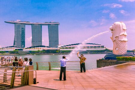 Man posing with a hat for a photograph at sunset next to the Merlion at the Merlion Park in Singapore, Asia with the Marina Bay Sands hotel in the backgroundのeditorial素材
