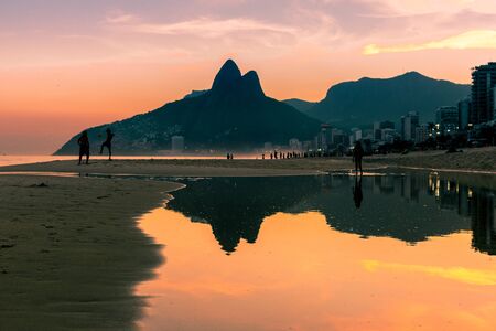 Reflection of Dois IrmÃ£os (Two Brothers) mountains at sunset in a puddle on Ipanema beach with...