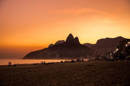 Ipanema beach with silhouette of people relaxing & having fun at sunset with Dois IrmÃ£os (Two Brothers) mountains in background in Rio de Janeiro, Brazil, South Americaのeditorial素材