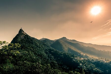 Christ the Redeemer (Cristo Redentor) on Mount Corcovado during beautiful sunset with mountains, forest & a bird flying past the sun in Rio de Janeiro, Brazil, South Americaのeditorial素材