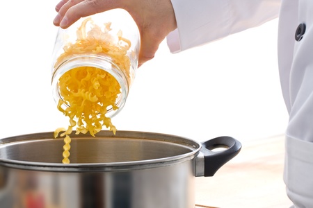 Male chef adding pasta into pot over white backgroundの写真素材