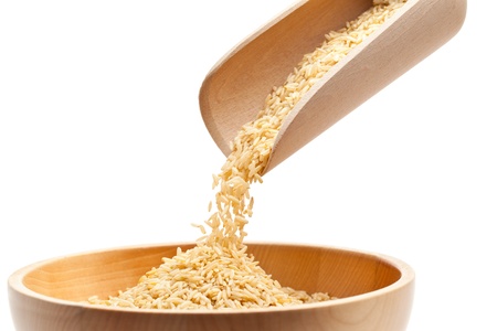 Raw organic brown rice filled into wooden bowl over white backgroundの写真素材