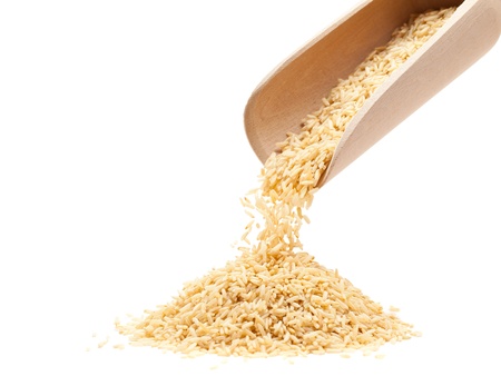 Raw organic brown rice poured from wooden scoop over white backgroundの写真素材