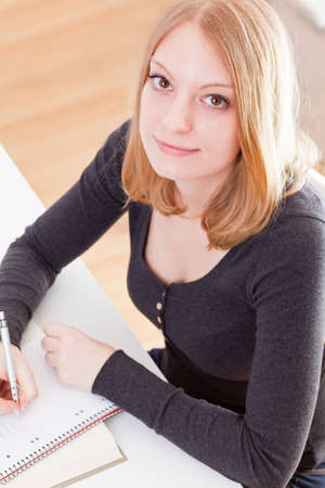 Young female student doing her homework at the tableの写真素材