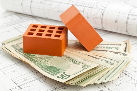 Brick stones with dollar banknotes on home construction blueprints - home or construction financing conceptの写真素材