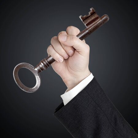 Hand holding key over black background - key to success or achievement conceptの写真素材