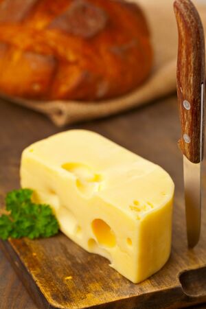 Piece of fresh organic edam cheese on wooden board with fresh bread on breakfast kitchen tableの写真素材