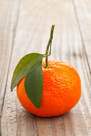 Single whole organic tangerine wit green leaves on wooden tableの写真素材