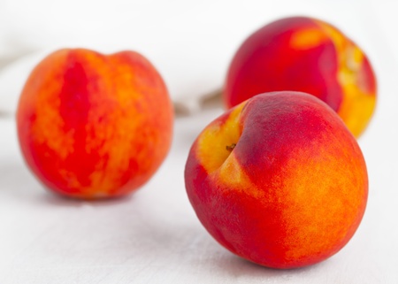 Three fresh organic whole peaches on white wooden cutting boardの写真素材