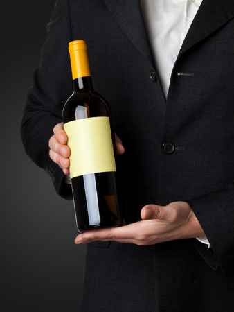 Man in suit holding white wine bottle isolated on black backgroundの写真素材