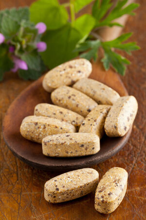 Herbal vitamin and supplement pills with herbs on wooden spoonの写真素材
