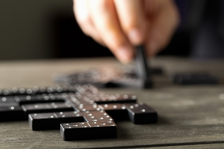 Game of domino with domino stones on wooden background with man about to make a move; selective focus on domino stone in frontの写真素材
