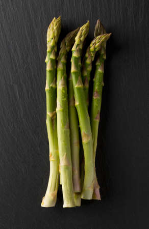 Bundle of fresh cut raw, uncooked green asparagus vegetable on black stone boardの写真素材