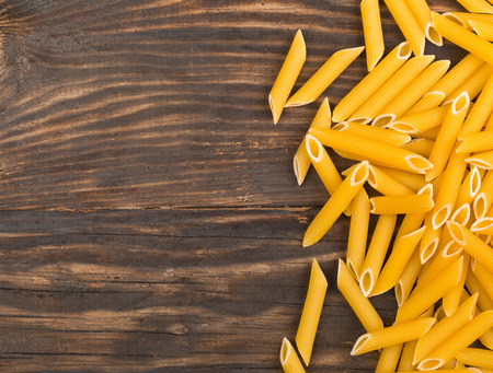 Raw, uncooked, dry penne pasta noodles border on rustic brown wooden table with copy spaceの写真素材