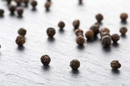 Raw, natural, unprocessed black pepper peppercorns macro on dark stone background with selective...