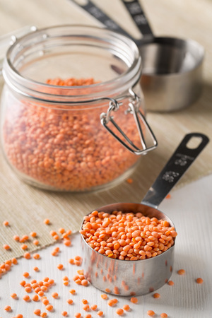 Raw red, dried  lentils in metal measurement scoop and glass storage jar on kitchen tableの写真素材