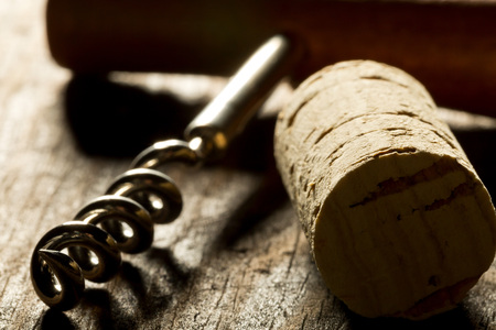 Corkscrew with wooden handle and corks from wine bottles on wooden table backlit