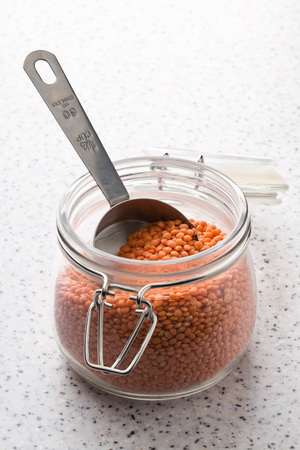 Raw red, dried  lentils in metal measurement scoop and glass storage jar on kitchen tableの写真素材