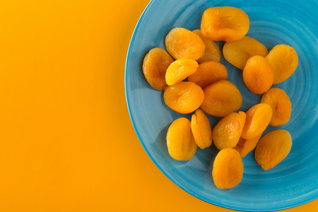 Whole dried apricots fruit on cyan plate on orange background from aboveの写真素材